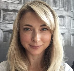 A woman with shoulder length blonde hair and blue eyes is smiling and looking at the camera.